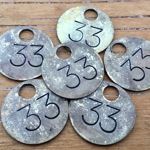 May include: Six brass tags with the number 33 engraved on them. The tags are round and have a hole in the top for attaching them to something.