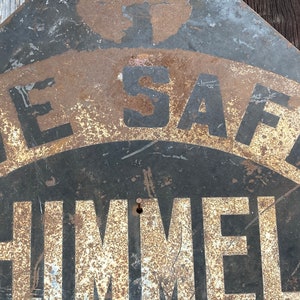 May include: A weathered metal sign featuring the text "LIVE SAFE" and "HIMMEL" in black and white. The sign has a distressed, rusty finish, indicating it's an older piece. The sign's design suggests it's an antique or vintage item.