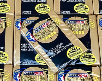 Puede incluir: Una pila de paquetes de cartas de baloncesto Fleer 1992-93 sin abrir con Larry Johnson, el "NBA Rookie of the Year". Los paquetes son dorados con un gráfico de baloncesto y el texto "Fleer 92-93 Basketball Cards".