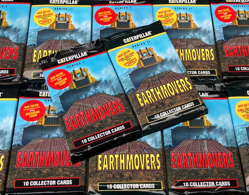 May include: A close-up of a stack of sealed packs of Caterpillar Earthmover trading cards. The packs are black with yellow and red accents. The text on the packs reads "Caterpillar Earthmovers 10 Collector Cards".