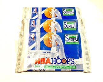 May include: Three packs of 1992-93 NBA Hoops basketball trading cards. Each pack contains 12 cards. The packs are sealed and feature a blue and white design with a basketball player and a basketball.