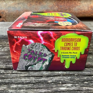 Puede incluir: Una caja de cartas coleccionables de Tales from the Crypt. La caja es roja y verde con una imagen de una l&aacute;pida que dice "Tales from the Crypt". El texto en la caja dice "Horrorvision Comes to Trading Cards" y "36 Packs".