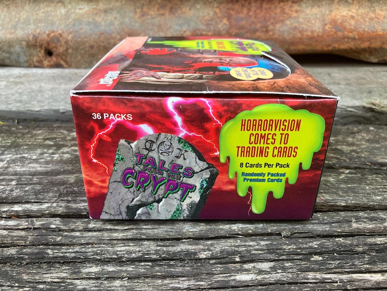Puede incluir: Una caja de cartas coleccionables de Tales from the Crypt. La caja es roja y verde con una imagen de una l&aacute;pida que dice "Tales from the Crypt". El texto en la caja dice "Horrorvision Comes to Trading Cards" y "36 Packs".