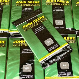 May include: A close-up of multiple sealed packages of John Deere Collector Cards. The packages are green and black with the John Deere logo and the text "Limited Edition 1994 Series".