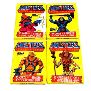 May include: Four yellow card packs featuring characters from the Masters of the Universe cartoon. Each pack has a different character: Skeletor, He-Man, Beast Man, and Teela. Each pack says "10 Cards - 1 Sticker - 1 Stick Bubble Gum".