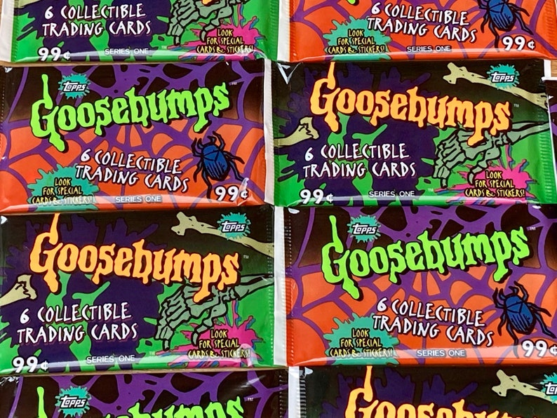 K&ouml;nnte beinhalten: Vier Packungen Goosebumps Sammelkarten. Jede Packung zeigt ein anderes gruseliges Bild, darunter ein Spinnennetz, eine Skeletthand und einen K&auml;fer. Die Packungen sind alle orange, gr&uuml;n und lila mit dem Text "Goosebumps" in gr&uuml;ner und orangefarbener Schrift. Jede Packung enth&auml;lt 6 Sammelkarten und kostet 99 Cent.
