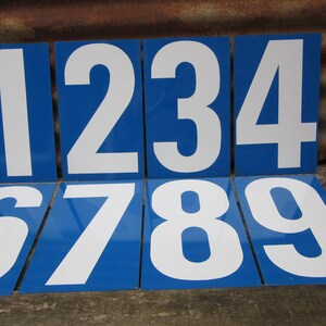 May include: Nine blue and white number signs with white numbers on a blue background. The numbers are 0, 1, 2, 3, 4, 5, 6, 7, 8, and 9.