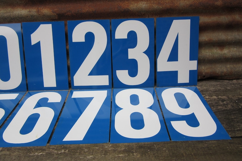 May include: Nine blue and white number signs with white numbers on a blue background. The numbers are 0, 1, 2, 3, 4, 5, 6, 7, 8, and 9.