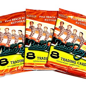 May include: Three sealed trading card packs featuring The Beach Boys. Each pack has a vibrant orange and yellow design with the band's image and the text "Find Beach Boys Autographs." The packs also state "8 Trading Cards."