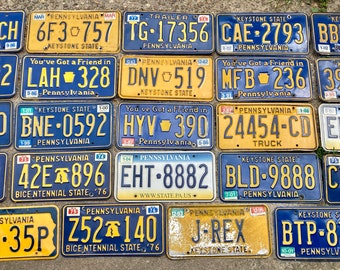 May include: A collection of vintage Pennsylvania license plates with various designs and slogans. The plates are yellow with blue lettering and feature the state's name, a keystone symbol, and a variety of slogans, including "You've Got a Friend in Pennsylvania" and "Bicentennial State '76".