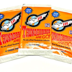 May include: Three orange foil trading card packs featuring the Thunderbirds Are Go logo, the Pro Set brand name, and the text The only official Thunderbirds Collection. Each pack displays a 25P price tag and indicates that there are 6 cards per pack.