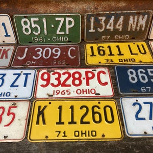 May include: A collection of vintage Ohio license plates with various numbers, letters, and years. The plates are in different colors, including white, yellow, blue, red, and green. Some of the plates have faded paint and rust.