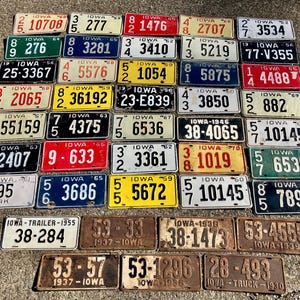 May include: A collection of vintage Iowa license plates from different years. The plates are in various colors and conditions, with some showing signs of wear and tear. The plates feature different numbers and letters, as well as the state name "Iowa" and the year of issue.