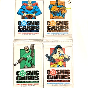 May include: Four unopened packs of DC Comics Cosmic Cards trading cards. Each pack features a different superhero: Superman, Deathstroke, Green Lantern, and Wonder Woman. The packs are white with a blue and red DC Comics logo and the text "Cosmic Cards" in black. Each pack says "Inaugural Edition" and "Bonus Holograms Randomly Inserted!"
