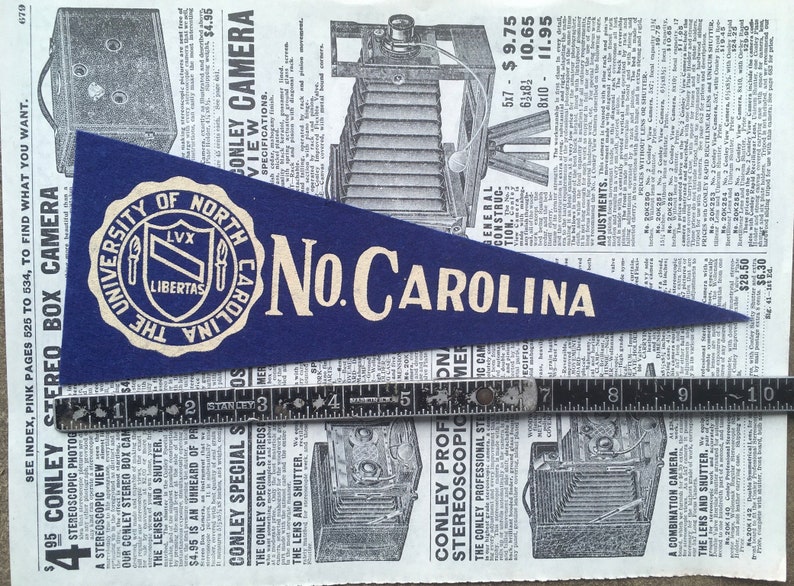 Puede incluir: Un bander&iacute;n azul de fieltro con letras blancas que dicen "The University of North Carolina No. Carolina". El bander&iacute;n presenta un escudo blanco con un escudo y las palabras "LVX LIBERTAS".