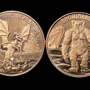 May include: Two bronze-colored coins. One coin features a winged creature with the text "THE JERSEY DEVIL". The other coin depicts a large, hairy humanoid with the text "ABOMINABLE SNOWMAN".