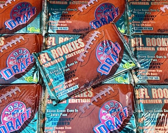 Puede incluir: Primer plano de varios paquetes sellados de tarjetas de intercambio de la NFL Draft de 1995. Los paquetes son de diferentes colores y presentan una variedad de imágenes, incluidos jugadores de fútbol americano y el logotipo de la NFL. El texto en los paquetes dice "1995 NFL Draft" y "Premier Edition".