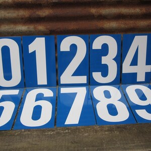 May include: Nine blue and white metal number plaques, each with a white number on a blue background. The numbers are 0 through 9.