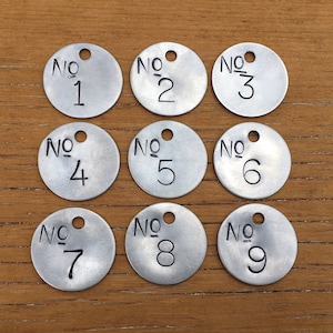 May include: Nine silver metal tags with rounded edges and holes at the top. Each tag has a black number from 1 to 9 and the text "No." above the number.