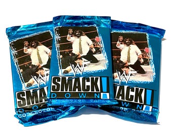 May include: Three blue-wrapped packs of "SmackDown Collector Cards" are shown. Each pack features a wrestler in a white shirt and tie. The packs have the WWE logo and the words "SmackDown Collector Cards".