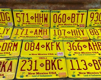 May include: A collection of ten yellow license plates from New Mexico, USA. Each plate features a red number and letter combination, a red star symbol, and the text "New Mexico USA Land of Enchantment".