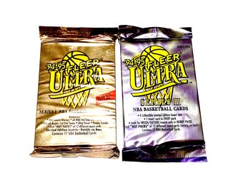 May include: Two unopened packs of 1994-95 Fleer Ultra NBA basketball cards. One pack is gold and the other is purple. The gold pack is Series I and the purple pack is Series II. Each pack features a basketball graphic.