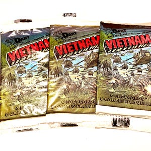 May include: Three sealed packs of trading cards featuring a cartoon illustration of soldiers in a jungle setting. The packs are labeled "Dart Flipcards Presents Vietnam" and "6 Fact Cards".