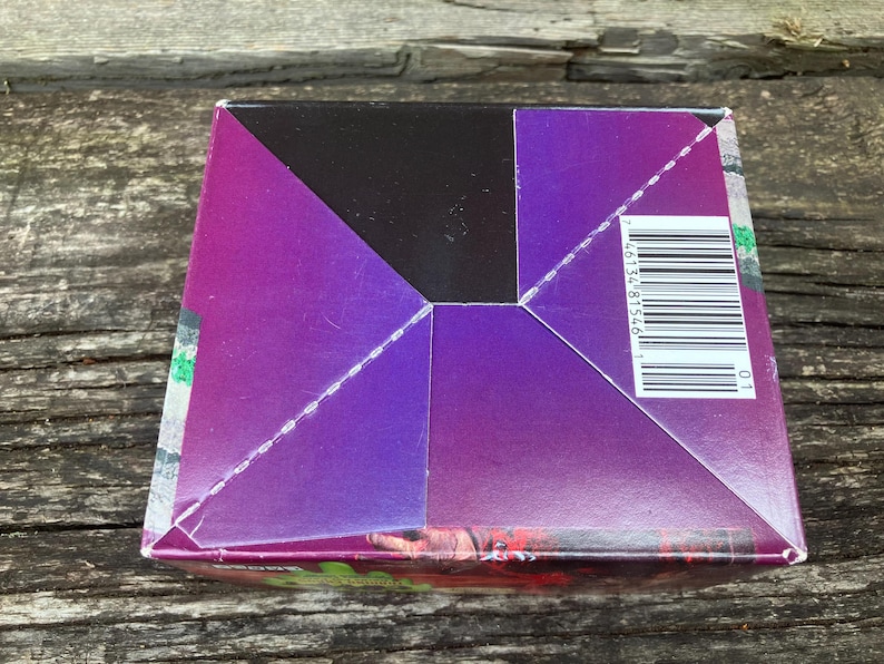 Puede incluir: Una caja de color morado, negro y verde con un c&oacute;digo de barras y el n&uacute;mero "46134 81546 1" impreso en el lateral.