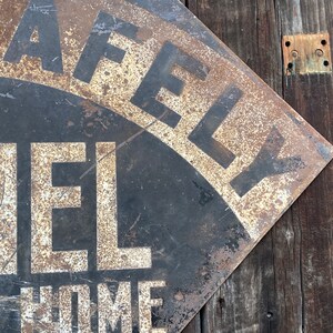 May include: A distressed metal sign with the words "SAFELY" and "MEL" in white lettering on a black background. The sign is mounted on a wooden surface, showing signs of rust and age.