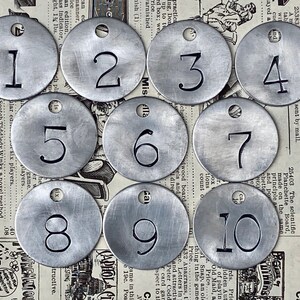 May include: Ten silver metal tags with numbers 1 through 10 printed on them. The tags have a hole punched in the top.