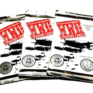 May include: Three sealed trading card packs. Each pack features a red and white graphic with the text "A Grateful Nation Remembers Trading Cards". Silhouettes of airplanes and bombs are visible. The packs are silver and white.