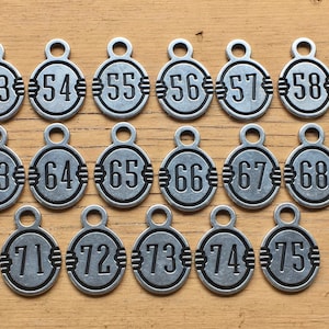 May include: A set of 15 silver-toned metal tags with black numbers from 53 to 75. The tags are circular and have a small loop at the top for attaching.