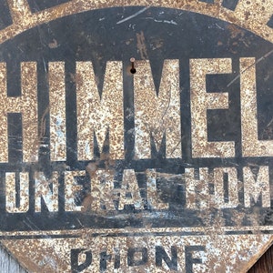 May include: A distressed, fan-shaped metal sign for "Himmel Funeral Home." The sign features black paint with white lettering and a rusty finish. The words "Funeral Home" and "Phone" are also visible.