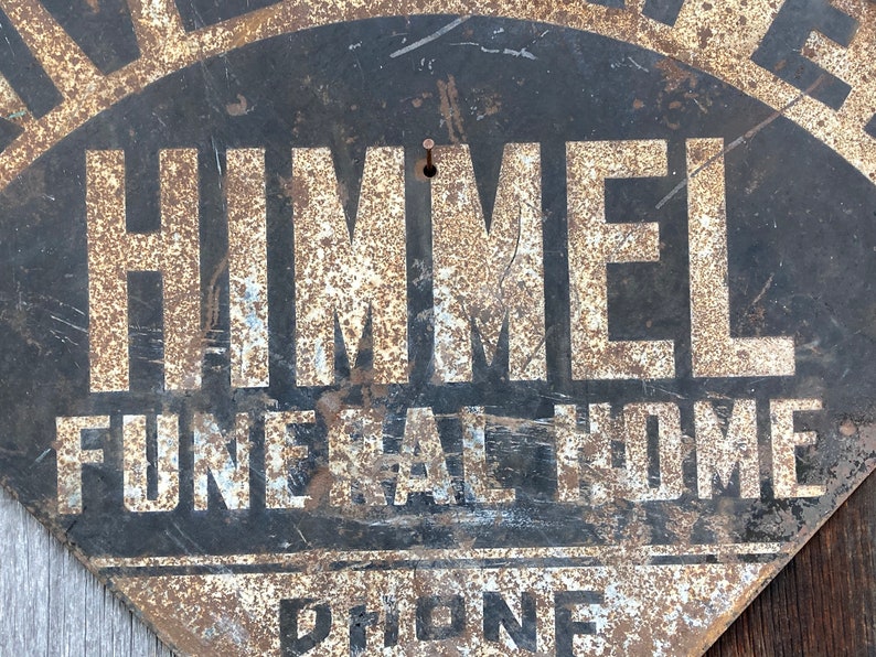 May include: A distressed, fan-shaped metal sign for "Himmel Funeral Home." The sign features black paint with white lettering and a rusty finish. The words "Funeral Home" and "Phone" are also visible.