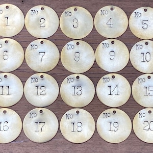 May include: Twenty round brass tags with a hole at the top. Each tag is numbered from 1 to 20. The tags are arranged in four rows of five tags each.