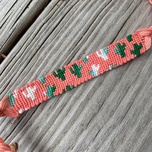 Pode incluir: Um bracelete de amizade rosa, verde e branco com um padrão de cacto.