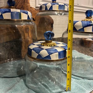 May include: Clear glass jars with blue and white checkered lids and gold trim. The jars have blue glass knob handles. The height of the jar is approximately 6 inches.