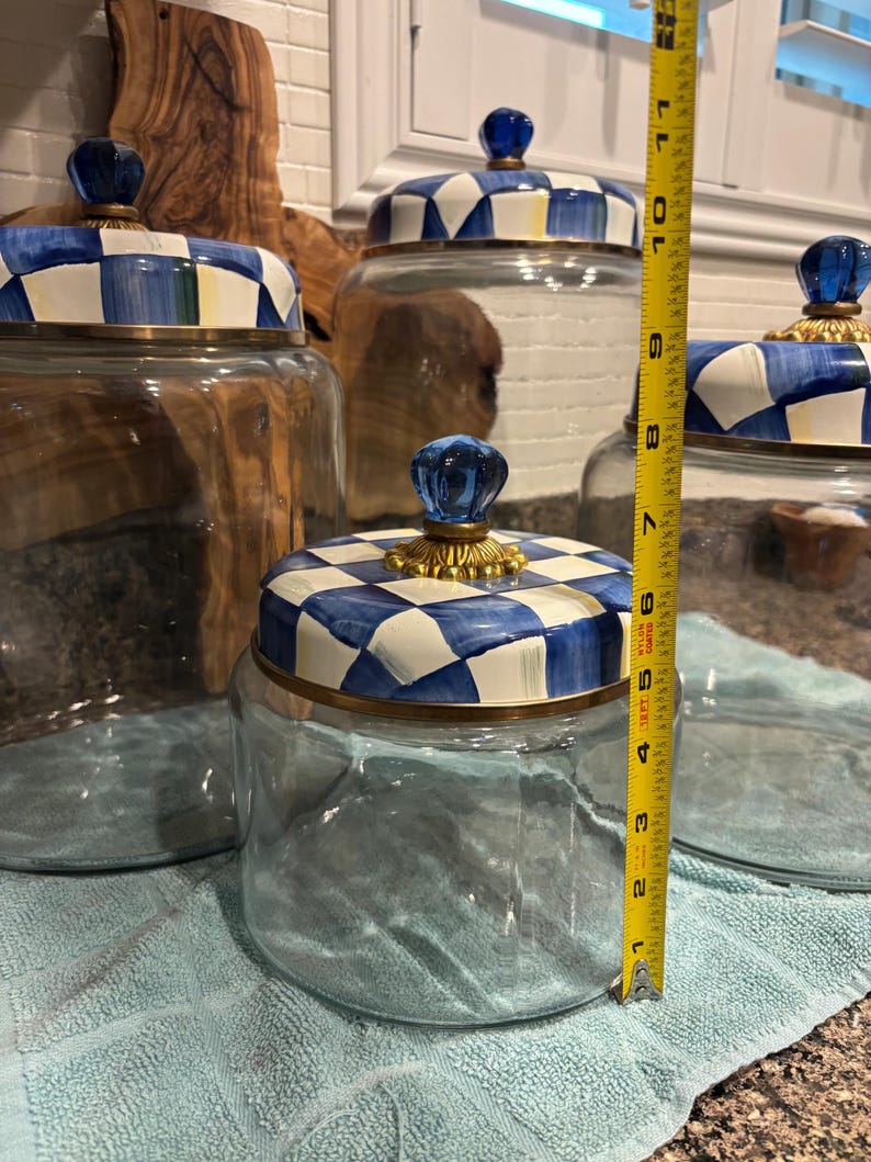 May include: Clear glass jars with blue and white checkered lids and gold trim. The jars have blue glass knob handles. The height of the jar is approximately 6 inches.