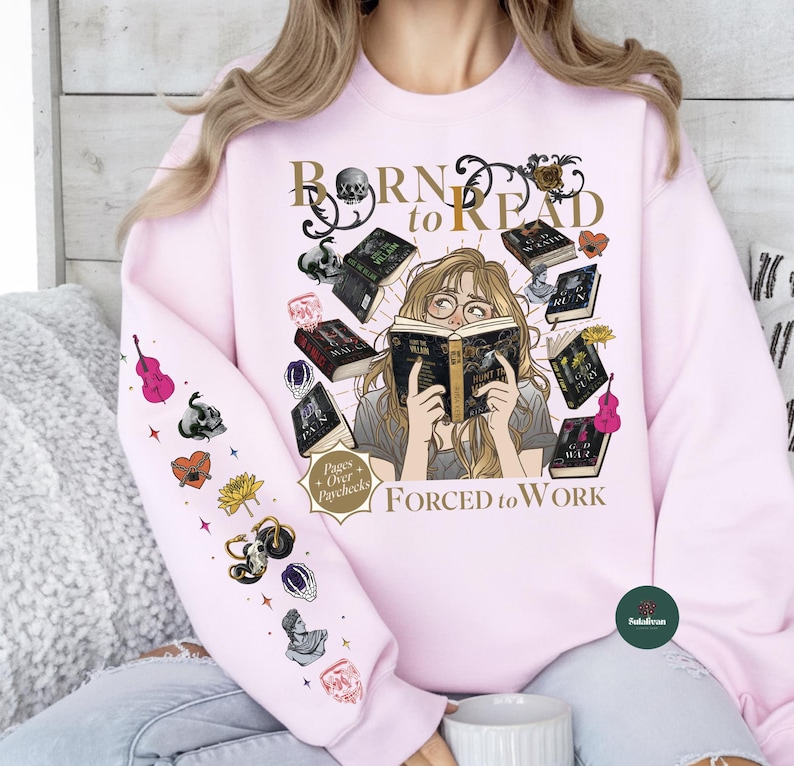 May include: Light pink sweatshirt with the text "Born to Read" and "Forced to Work". The graphic features a woman reading surrounded by books and decorative elements. The left sleeve has various illustrations.