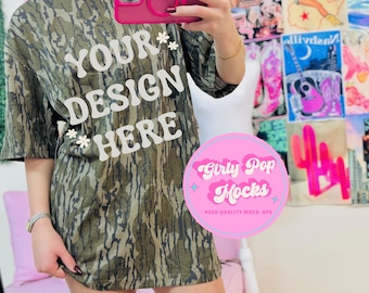 Könnte beinhalten: Olivgrünes Tarnmuster-T-Shirt mit dem Text "YOUR DESIGN HERE" in Weiß. Das Shirt hat eine lockere Passform und kurze Ärmel. Das Bild enthält auch eine pinke Handyhülle und ein "Girly Pop Mocks"-Logo.