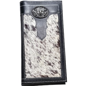 Peut inclure: Un long portefeuille à deux volets avec un motif de peau de vache dans les tons de blanc, marron et noir. Le portefeuille présente une bordure en cuir noir avec des coutures blanches et un emblème décoratif en métal argenté. Le portefeuille est rectangulaire.
