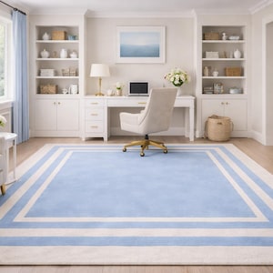 Könnte beinhalten: Ein rechteckiger Teppich in Hellblau und Weiß mit einem Bordürendesign. Der Teppich befindet sich in einem Raum mit weißen Möbeln, einem Schreibtisch und einem Stuhl. Der Raum hat ein Fenster mit hellblauen Vorhängen.