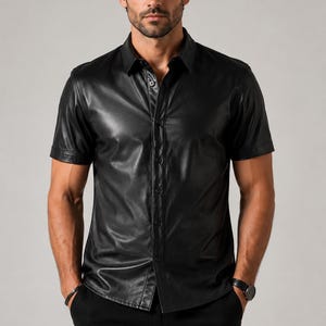 May include: A short-sleeved black button-down shirt with a smooth, reflective finish. The shirt features a classic collar, a front button placket with matching black buttons, and a straight hemline. The material has a distinct sheen.
