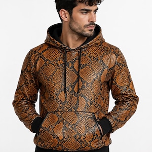 May include: A long-sleeve hooded sweatshirt featuring a brown and black snakeskin pattern. The garment includes a front kangaroo pocket, black ribbed cuffs, a black ribbed hem, and black drawstring cords attached to the hood.