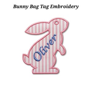 Könnte beinhalten: Besticktes Hasen-Gepäckanhänger mit rosa-weißem Streifenmuster. Der Anhänger hat die Form eines Hasen mit dem Namen "Oliver" in blauer Stickerei. Der Text "Bunny Bag Tag Embroidery" steht über dem Hasen.