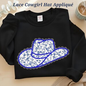 May include: Black sweatshirt with a floral cowboy hat appliqué. The hat has a blue and white floral design, a blue outline, and a white lace trim. The text "Lace Cowgirl Hat Appliqué" is at the top.