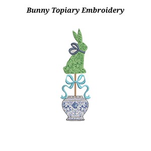 May include: Bunny Topiary Embroidery text above a green bunny topiary with a blue bow, atop a blue and white floral vase. The bunny is made of green embroidery and has a dark blue bow around its neck. A light blue bow is below the bunny.