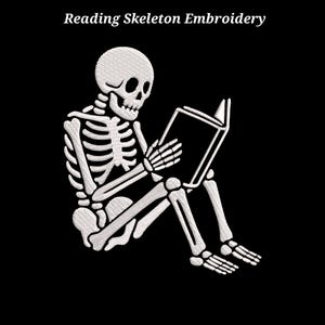 Op de afbeelding: Een wit borduurontwerp op een zwarte achtergrond met een skelet dat zit en een open boek leest. De tekst Reading Skeleton Embroidery staat in een wit schreeflettertype boven het skelet, wat zorgt voor een duidelijk visueel contrast.