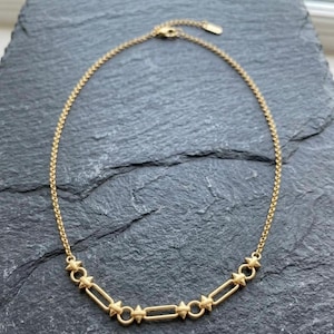 May include: A gold-toned necklace featuring a delicate chain that transitions into a series of alternating circular and elongated rectangular links, each accented with small, pointed stud details at the connection points and a secure clasp.