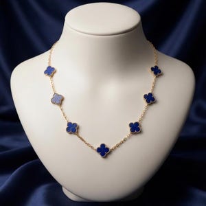 May include: A gold chain necklace featuring six evenly spaced, four-leaf clover-shaped charms. Each charm is inlaid with a deep blue stone and framed by a delicate gold beaded edge. The necklace is displayed on a smooth, neutral-toned bust.